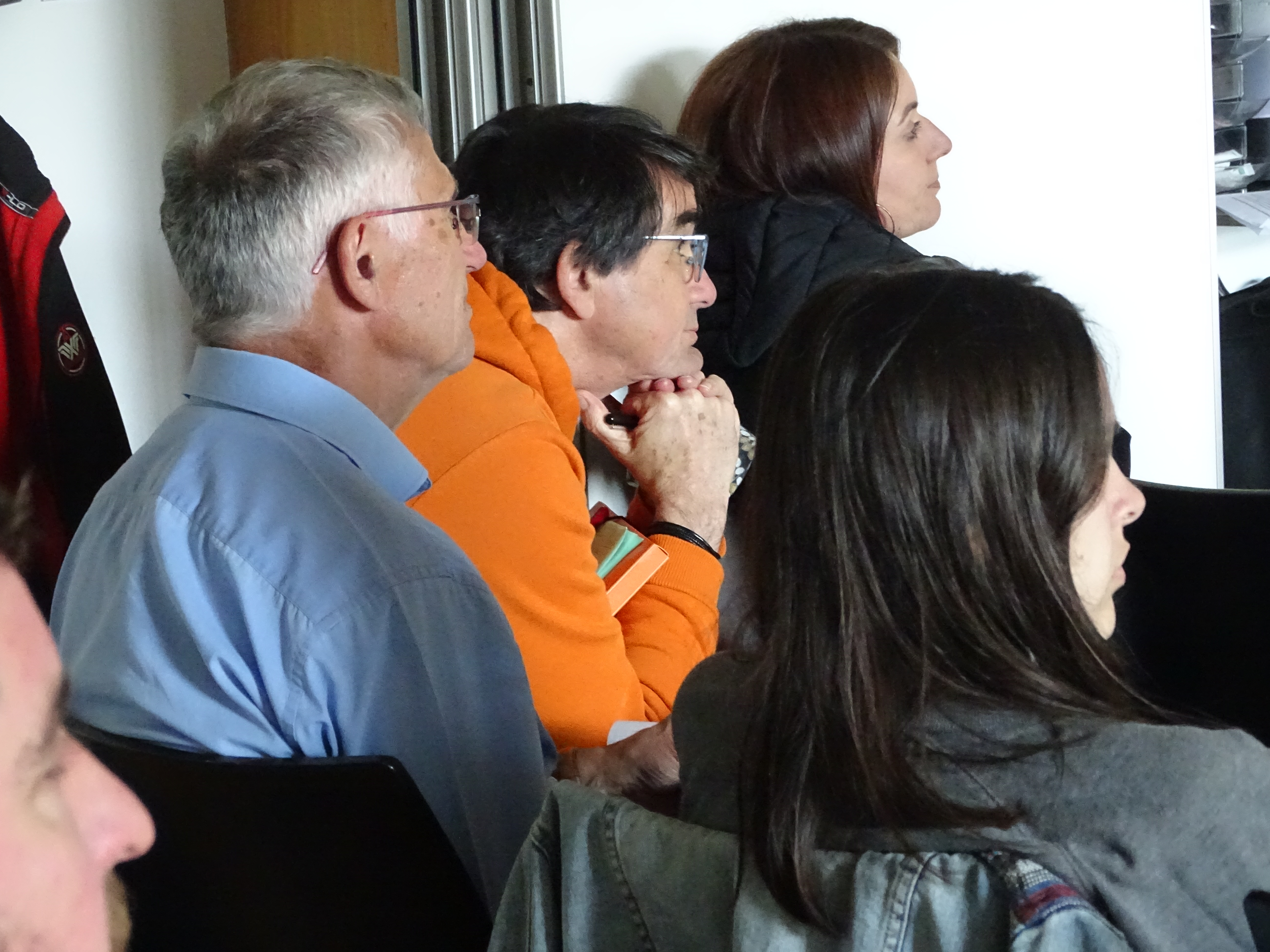 Personnes de 3 quarts dos assis sur des chaises à écouter quelqu'un parler