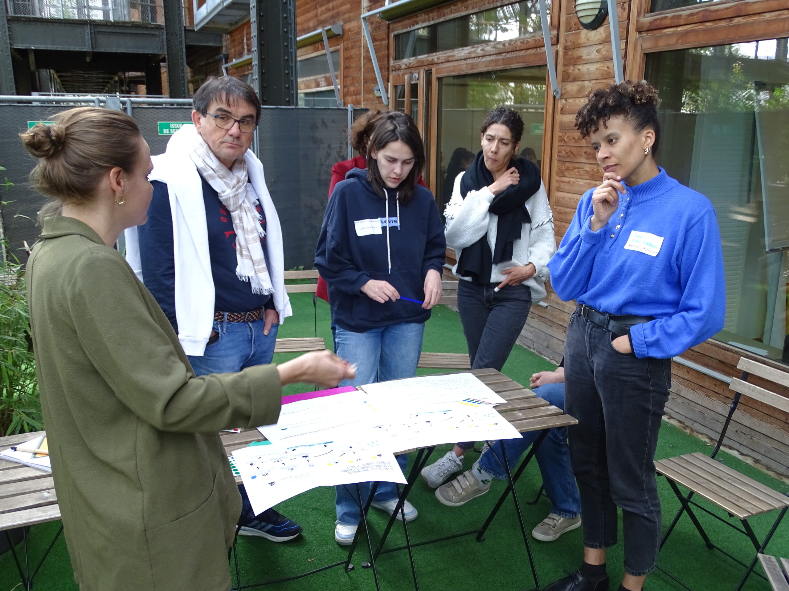 5 personnes réfléchissent debout autour d'une table sur laquelle sont disposées des feuilles 